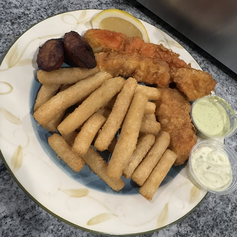 A Spanish dish with fried fish, plantains, yuca fries, a lemon wedge, and two dipping sauces.