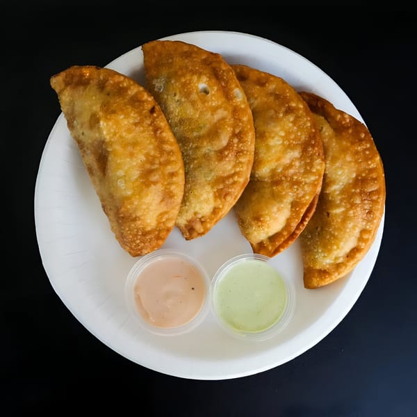 Four golden-brown empanadas and two dipping sauces on a white plate against a dark background.