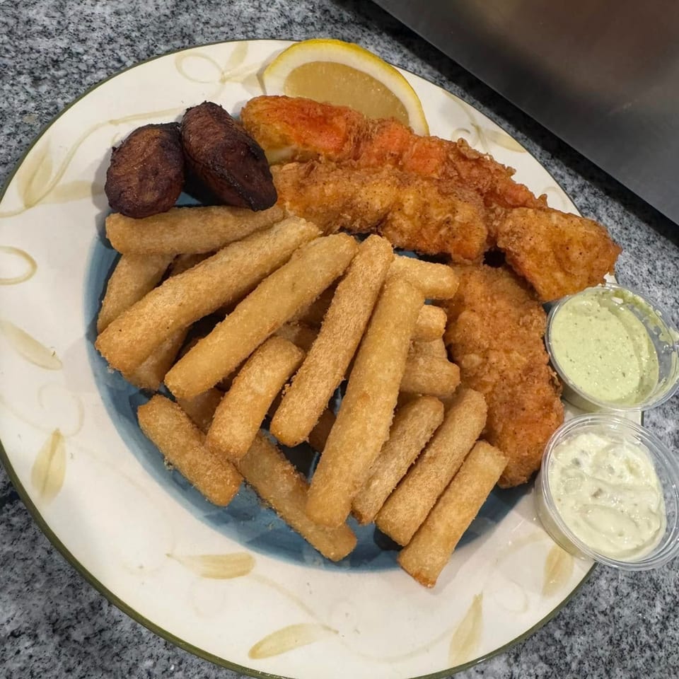 Fried fish, plantains, and fries with two dipping sauces and a lemon wedge on a plate.