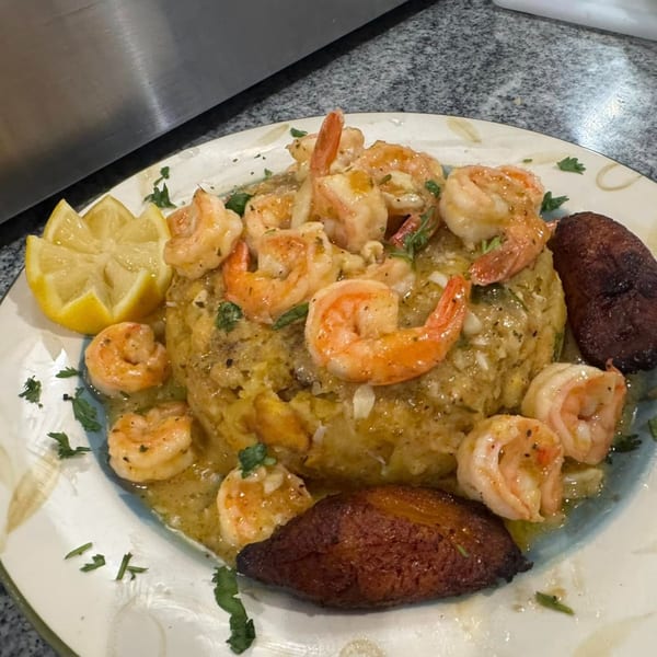El Gordo Coqui's Mofongo with shrimp, plantains, and a lemon wedge on a white plate.